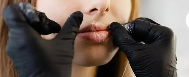 a sleek modern beauty salon interior, featuring a close-up of a professional aesthetician demonstrating the precise technique of facial threading on a client, illuminated by soft, warm lighting that enhances the tranquil and sophisticated atmosphere.