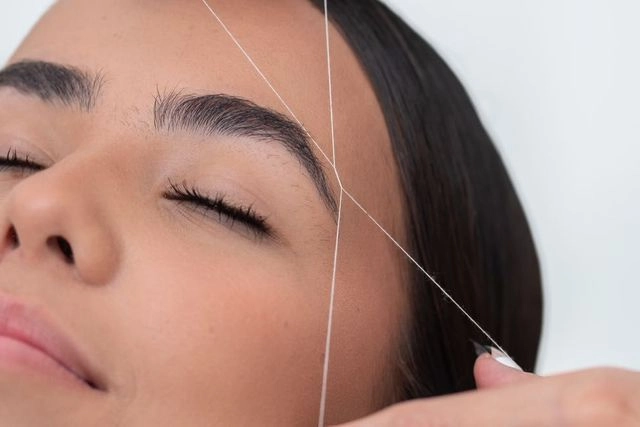 Macro view of precision eyebrow threading showing twisted cotton thread technique