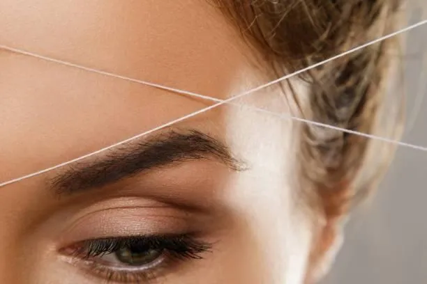 Expert esthetician mapping and shaping eyebrows with thread