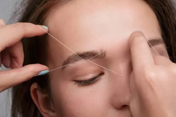 Esthetician shaping eyebrows with thread at Meena salon